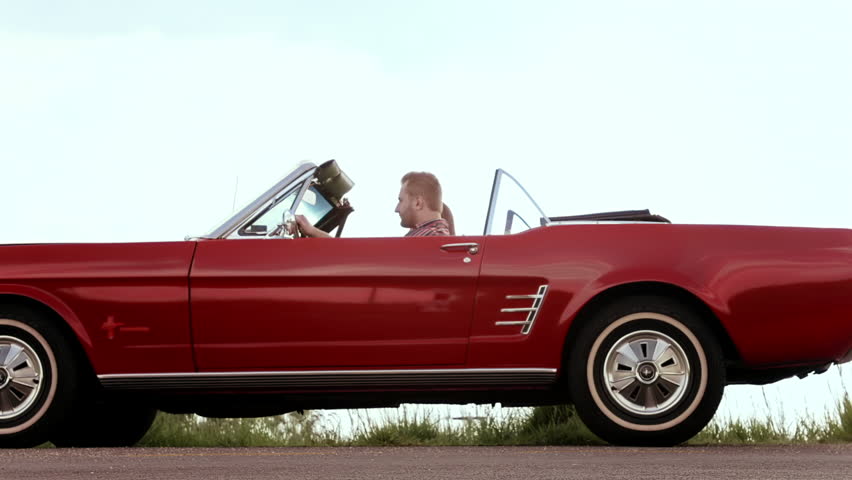 Couple have broken down with mechanical fault while driving a classic cherry red convertible, cabriolet car. 