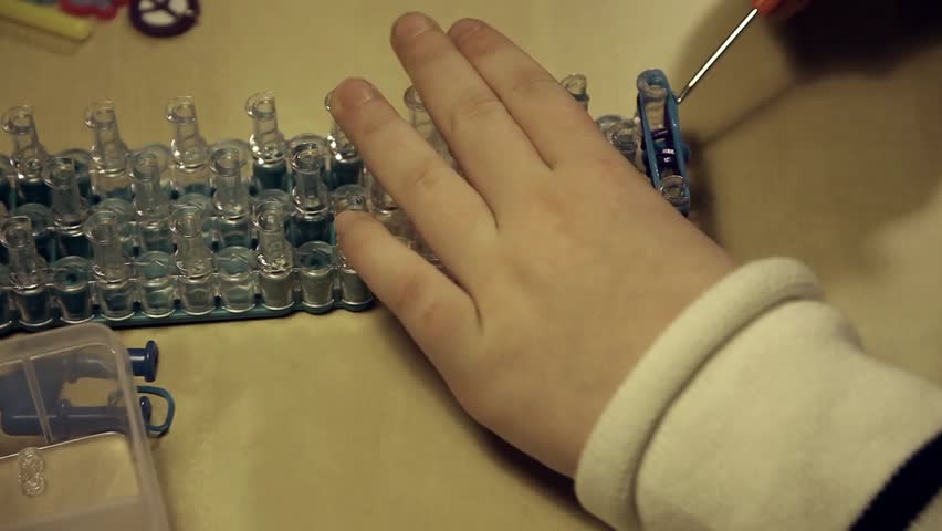 Girl is playing with Loom Bands and demonstrating her works.