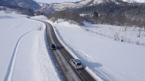 Aerial - Cars driving on a two-lane road through a snowy landscape
