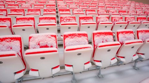 Rows of empty red seats on stadium tribune, covered by snow.