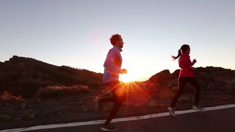 Running sport athletes woman and man jogging at night sunset. Runners training exercising on road in beautiful mountain landscape. Healthy lifestyle concept.