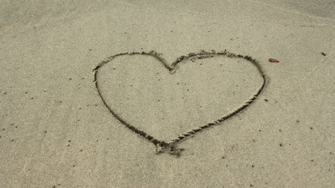 Heart drawn in sand gets washed away by wave