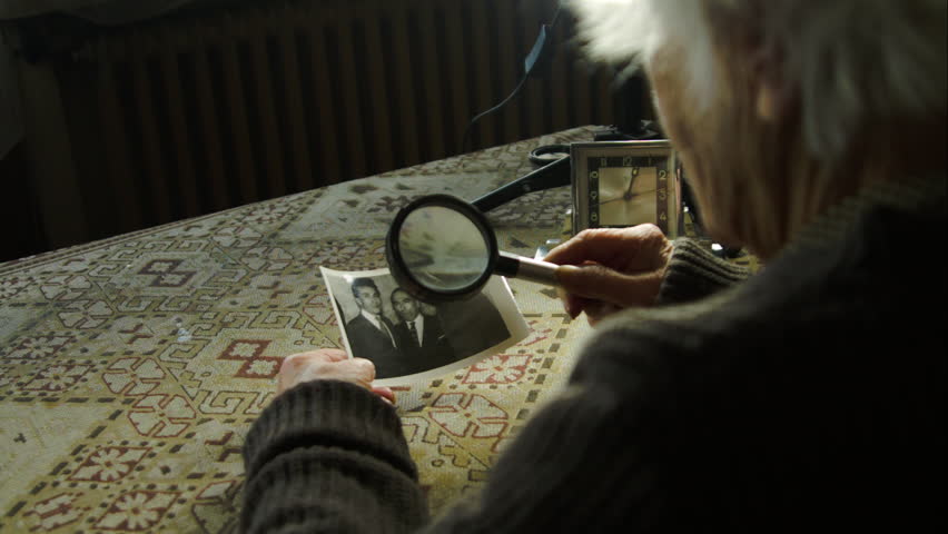 99 Years Old Woman Looking At an Old Photo With Magnifying Glass, Behind Shot