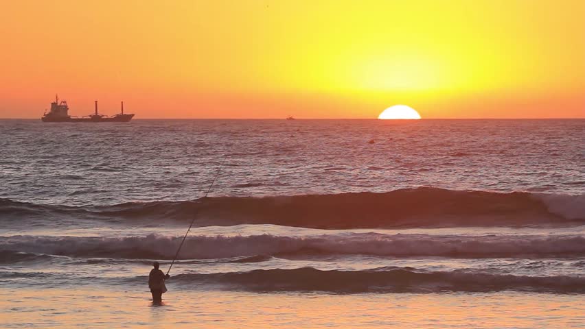 Moroccan fisherman fishing during sunset over Atlantic ocean. Composition include big ship on horizon and full sunset. Breath taking scenery of true Moroccan soul and flavor.