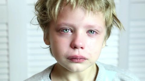 Head and shoulder portrait of caucasian blond boy crying and looking at camera and then closing his face with hands. Parenting, violence in family, bullying, feelings and emotions of children concept.