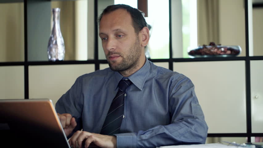 Friendly businessman with laptop talking good news to camera at home
