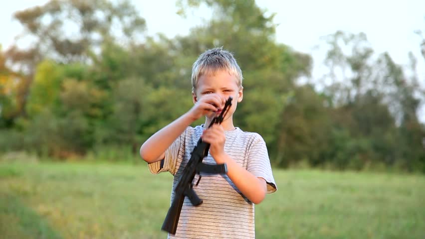 Cute boy shooting with toy gun. children toys. playing outdoors. baby in park. cheerful kid hiding behind bush. healthy lifestyle. handsome boy. war games. child play alone. violence
