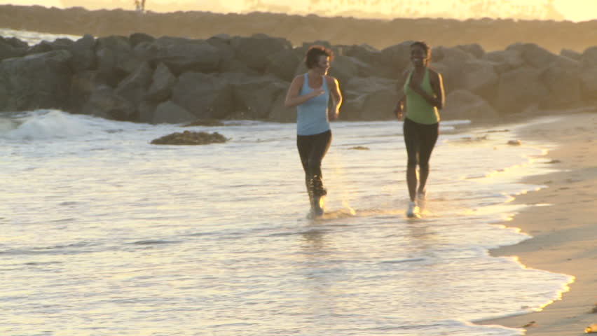 Two young women running along shore line at sunset