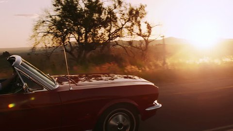 Couple driving classic cherry red convertible cabriolet car, steadicam shot with sun flare.