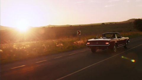 Couple driving classic cherry red convertible cabriolet car, steadicam shot with sun flare.