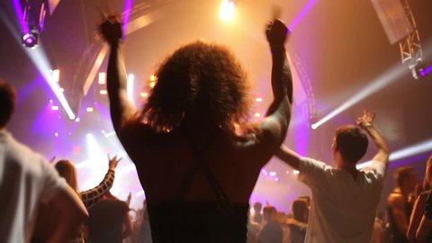 Back of young woman dancing in crowd in night club during big party