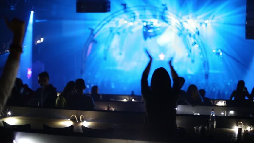 Laser show and silhouettes of back people clapping hands in night club during party