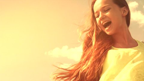 Beauty Joyful teenage girl having fun outdoors. Raising hands and blowing hair. Happy laughing teen girl over summer sky. Sunny day. Slow motion 240 fps. Slowmo. High speed camera shot