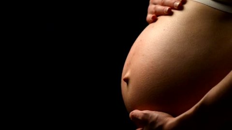 Pregnant woman tummy. Woman's hand caressing her nude pregnant belly, black background. Female hand on tummy of expectant mother. Gravid girl rubbing her big naked abdomen, close-up. HD 1920x1080p