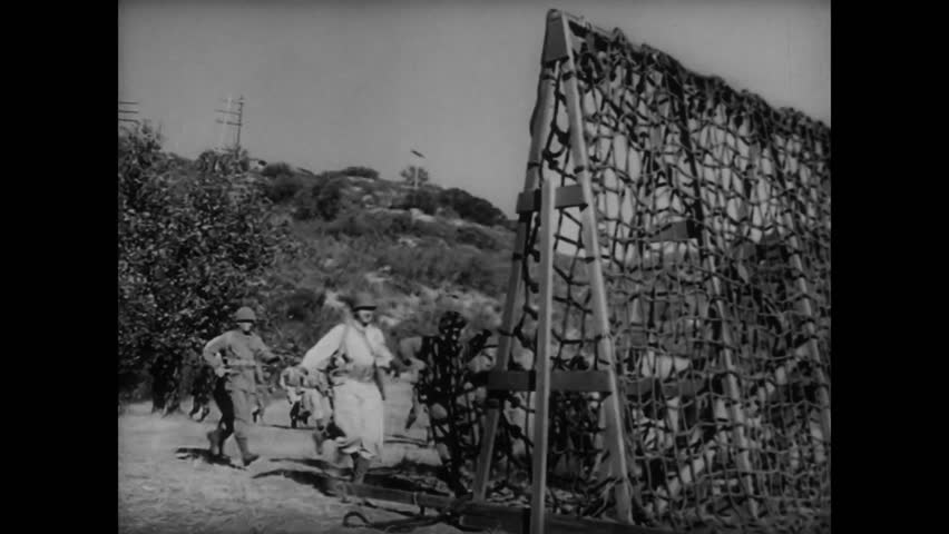 Large group of soldiers scaling rope ladder during training, 1940s