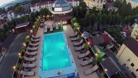 Man walks near pool and woman deeps in water on roof of hotel at summer evening. Aerial view