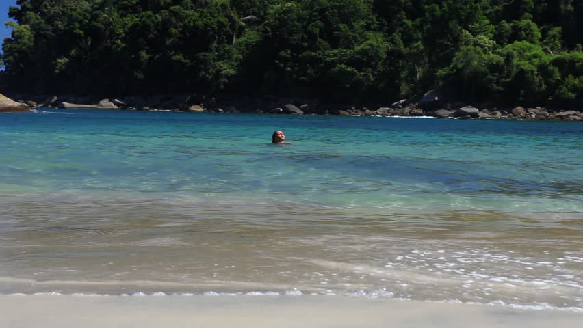 Young and beautiful looking woman coming out of crystal clear water, putting