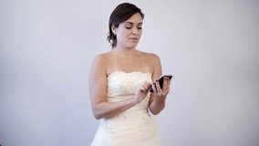 Indoor, studio shot, gray background of a happy bride to be on her wedding dress making a call on her cell phone