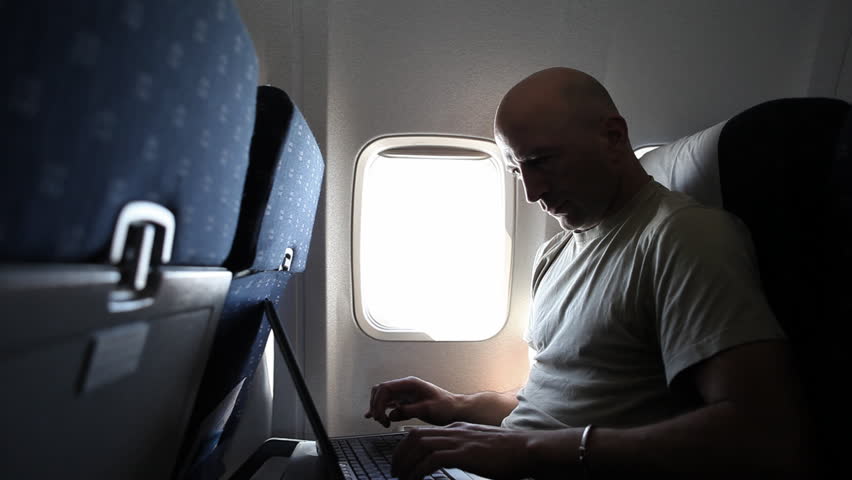 A middle-aged adult man is working with a laptop during a flight