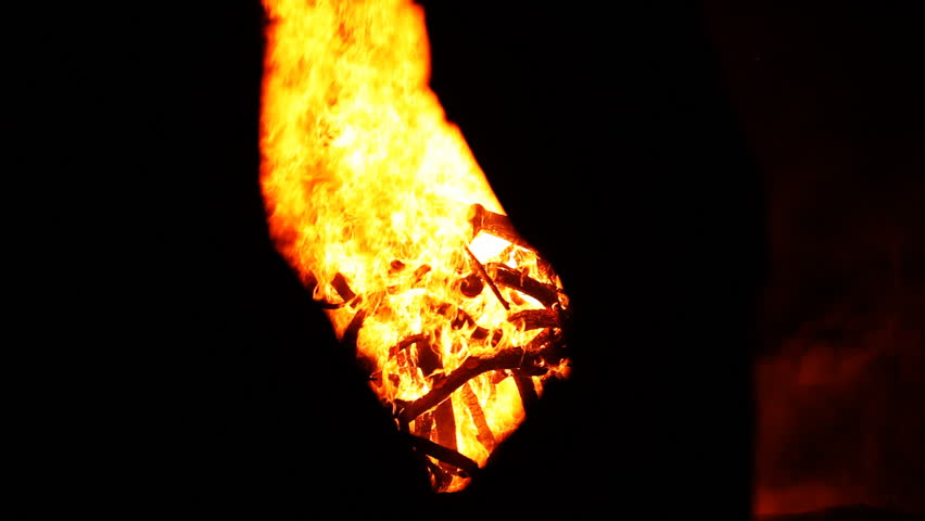 A huge sphere of wood is lit up and spreading high flames in front of black