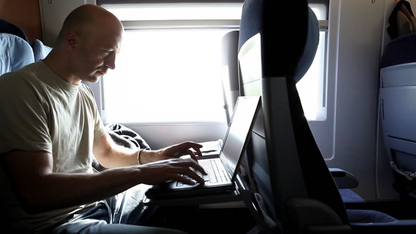 A middle-aged man is working with a laptop during a train ride, nice light