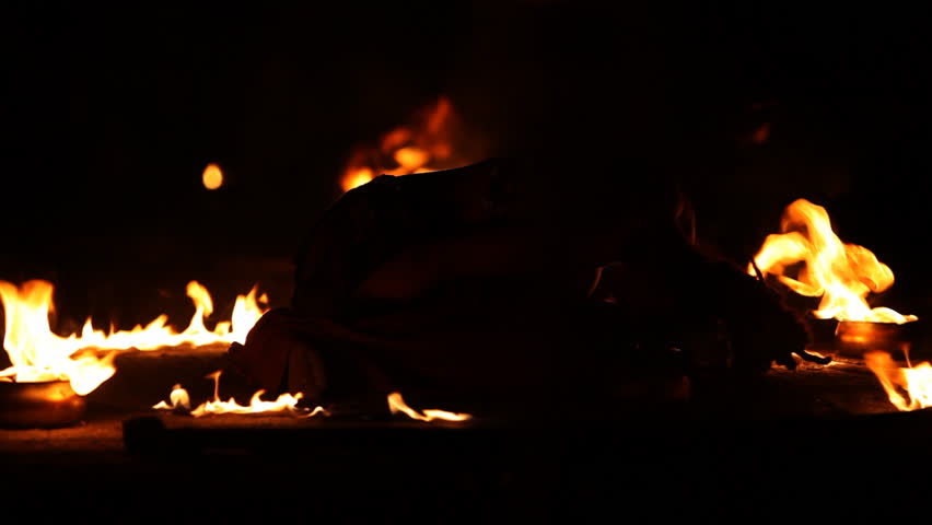 Several pots on the ground with burning fire surrounding a girl which is lying