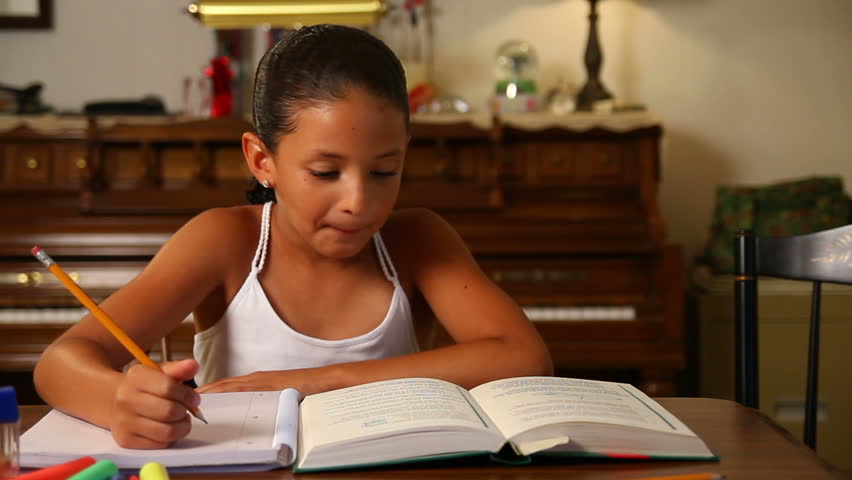 A young girl does her homework by herself in the dining room.