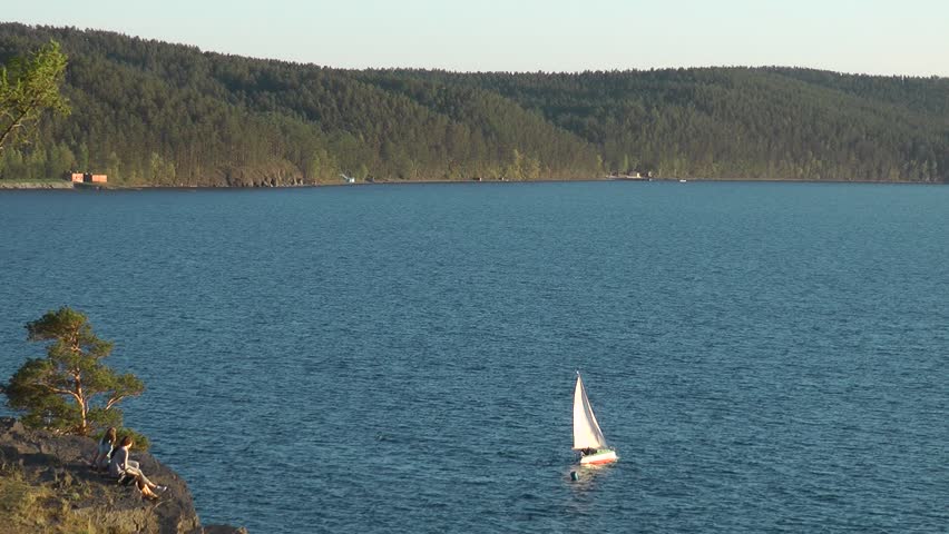 lake with yacht and rocks coastline, with two girls on cliffs