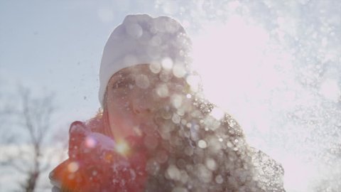 SLOW MOTION: Cheerful young woman blowing snowflakes into camera