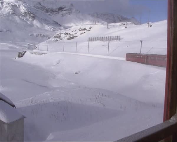 BERNINABAHN, SWITZERLAND - WINTER 1995: vehicle shot from riding train at rear wagon and mountain slope with snow fence. Bernina Railway, Switzerland, added to the list of UNESCO World Heritage Sites
