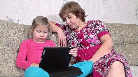 Grandma watching with interest how her granddaughter playing with tablet pc