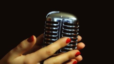 The seductive hands of a woman, a female singer, slowly caress a retro vintage shiny microphone on the stage. Close-up on black background.
 Stock Video