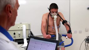 Fit man doing a stress test on exercise bike watched by doctor in high quality 4k format , Healthcare workers in the Coronavirus Covid19 pandemic - Powered by Shutterstock - Get 15% off with code: PIKWIZARD15
