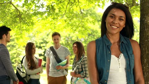 Portrait of happy mixed-race student posing and friends speaking behind her in the park of university