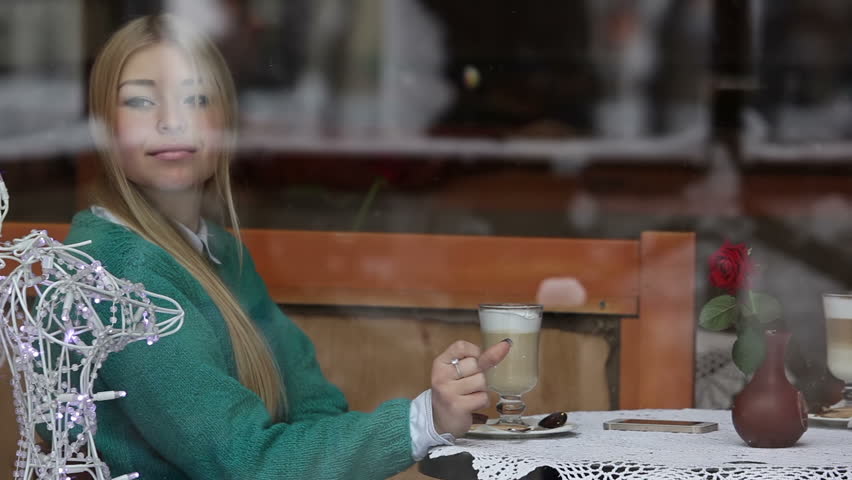 Girl in cafe drinks coffee latte and looks at phone