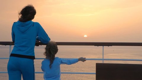 a mother and her little daughter watch the sun set from a ship