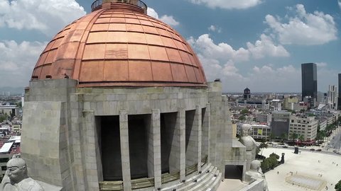 Aerial shot and close up of the dome of the Revolution Monument with the sky, clouds and city buildings on the back in a sunny day in Mexico City