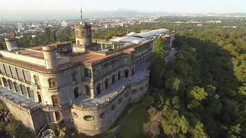Aerial top view of the Chapultepec Castle at the top of the hill with the forest surrounding it and a view of part of Mexico City behind in a very sunny morning