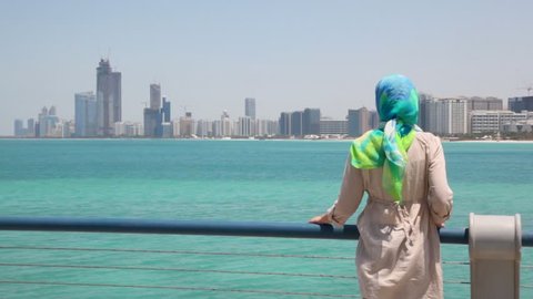 young woman stand on shore and looks at skyscrapers in Abu Dhabi, UAE