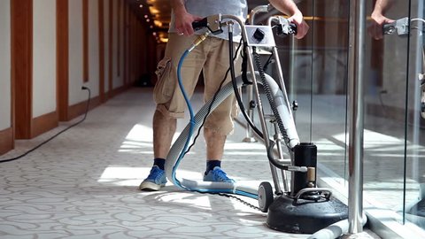 Cleaner male worker with carpet cleaning machine cleaning hotel corridor carpet.
Hotel carpet washing machine. Hotel cleaning service.