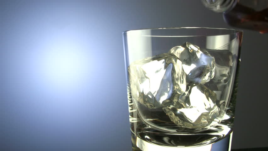 Closeup shot of scotch whiskey pouring into glass with ice cubes, includes space