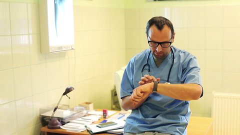 Young male doctor sitting with smartwatch in the hospital

