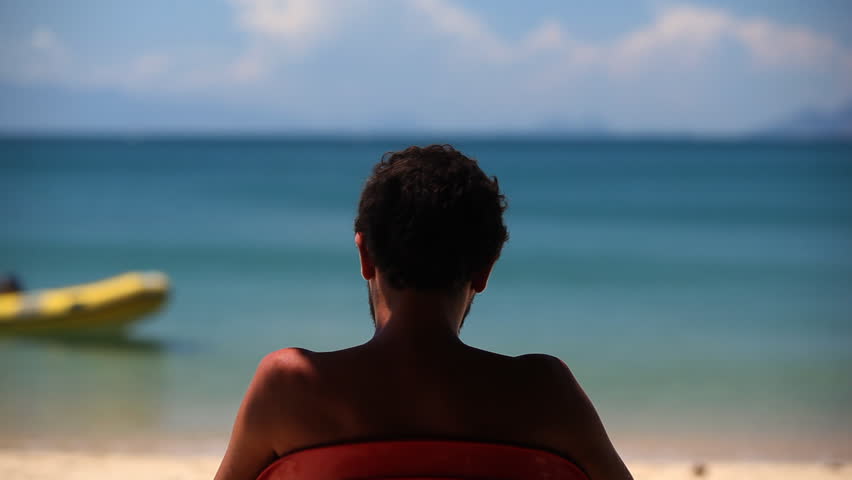 Man, shot from behind, sitting in front of beautiful turquoise water of a