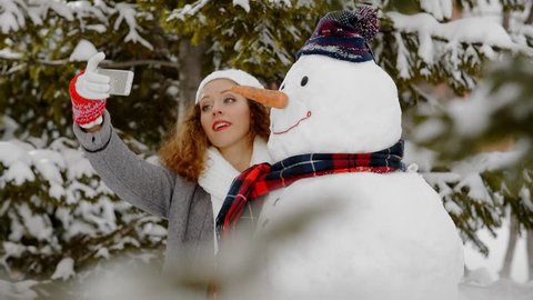 Pretty girl photographing with a snowman, winter selfie