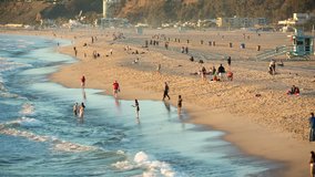 People Having Fun on Sandy Santa Monica Beach, Wading in the Ocean - Blue Water and Golden Brown Sand with Lifeguard Tower in Background - Waves Washing up on Shore in Los Angeles California