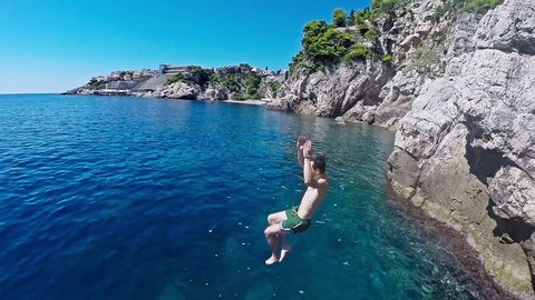 Athletic Young Man Jumping From Cliff Into Ocean Sea Water Muscular Adventure Extreme Sports Lifestyle Hobby Vacation Clear Beach Slow Motion Leisure Activity Gopro HD