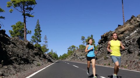 Sport fitness couple running. Runner man and woman jogging training on mountain road. Athletes runners working out for marathon on forest road in amazing nature landscape. Two models exercising.