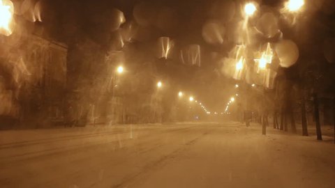 Snow-covered winter road from the windshield of the car at night in the light of the lamps and automobile headlights. Blizzard and heavy snowfall. Christmas and New Year weather