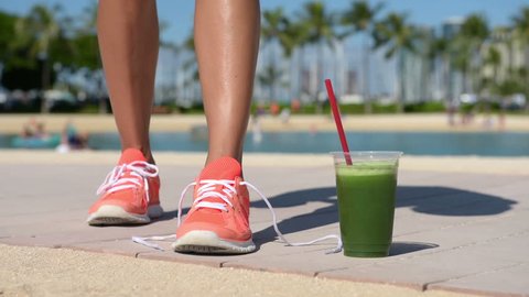 Running woman with green vegetable smoothie. Fitness runner and healthy lifestyle concept with female model tying running shoe laces.