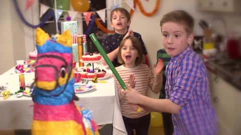 Boy hitting a pinata at party while his friends cheer him up in slow motion
